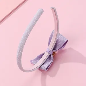 Détail d'un serre-tête à nœud violet avec couronne dorée et paillettes sur fond rose