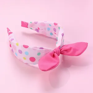 Détail d'un serre-tête en tissu rose avec pois colorés et gros nœud décoratif