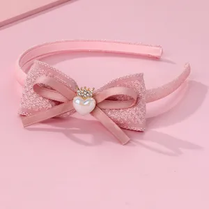 Détail d'un serre-tête rose pour fille avec double nœud, couronne et perle en cœur