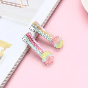 Dettaglio di fermagli per capelli arcobaleno glitterati con fiori 3D su sfondo rosa