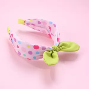 Détail d'un serre-tête rose à pois colorés avec un nœud décoratif vert vif