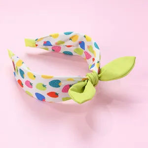 Détail d'un serre-tête motif fraises avec un nœud vert clair sur fond rose poudré