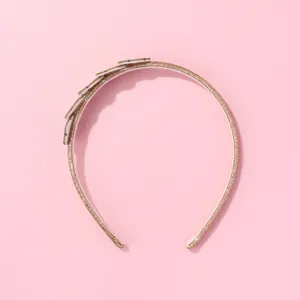 Detail eines schmalen Goldglitzer-Stirnbands mit runden Flicken auf rosa Hintergrund