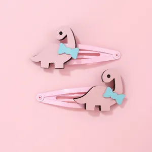 Détail de deux barrettes dinosaures roses avec nœuds bleus et texture en feutre