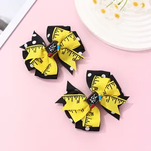 Detail of school-themed bow hair clips with yellow ruler print and ABC blackboard
