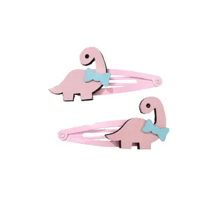 Détail de deux barrettes dinosaures roses en cuir texturé avec de petits nœuds bleus