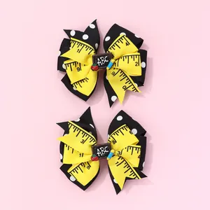 Detail of school-themed bow hair clips with yellow ruler print and ABC blackboard charm