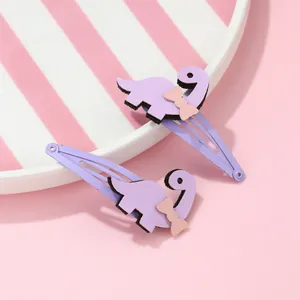 Détail de deux barrettes dinosaures violettes sur une assiette rose pour filles