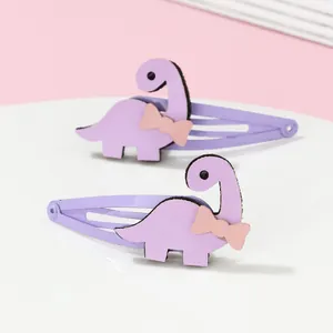 Détail de deux pinces à cheveux dinosaures violets avec de petits nœuds roses