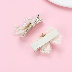 Détail de pinces à cheveux avec nœud en dentelle crème, couronne dorée et perle