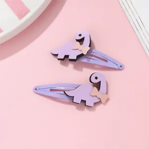 Détail de deux barrettes à cheveux dinosaure violettes sur un fond rose doux