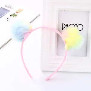 Detailed view of children's pink headband featuring soft gradient plush pom-poms on white