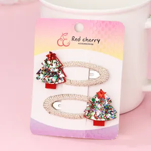 Detail of two Christmas tree hair clips with colorful sequins and gold thread on pink card