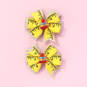 Detail of ruler-patterned yellow bow hair clips with miniature school books and apple