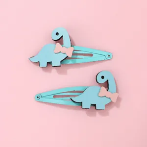 Détail de deux pinces à cheveux dinosaure bleu clair avec nœuds roses sur fond rose