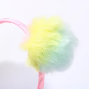 Close-up of a large fluffy rainbow gradient pom-pom detail on a pink ribbon headband