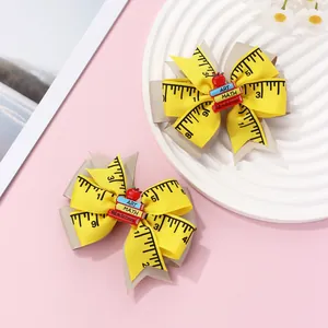 Detail view of yellow school-themed bow hair clips with ruler prints and mini books