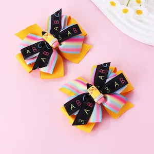 Détail de barrettes à nœuds jaunes scolaires avec rubans ABC arc-en-ciel et breloques crayon