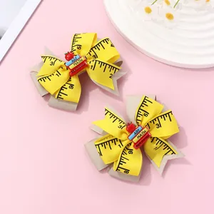 Detail of school-themed bow hair clips featuring ruler patterns, books, and red apples