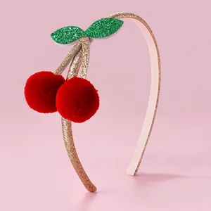 Dettaglio di ciliegie in pompon rosso e foglie glitterate su un cerchietto luccicante