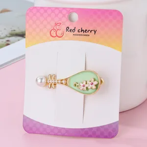 Close-up of pipa-shaped hair clip with enamel flowers and large pearl on brand card