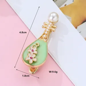 Macro shot of gold lute-shaped hair clip with dimensions 4.8cm by 1.8cm on pink background