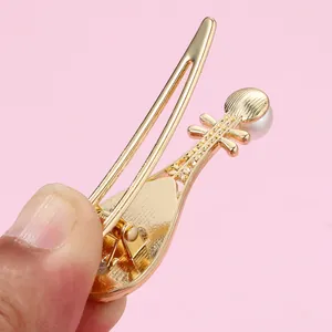 Close-up of golden pipa-shaped hair clip with faux pearl and spring metal mechanism