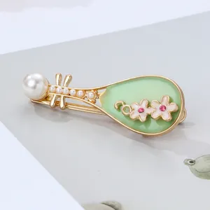 Macro shot of Pipa brooch with green enamel, faux pearls, and floral rhinestone details