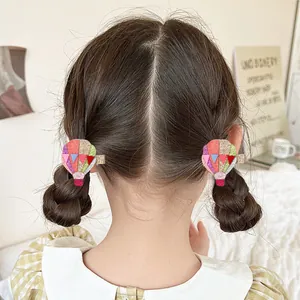 Detail of glitter hot air balloon hair clips worn on a child's braided pigtails