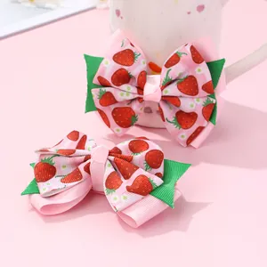 Close-up of pink bow hair clips with strawberry print and green leaf detail for girls