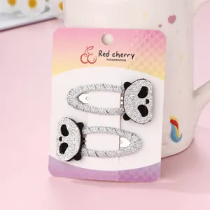 Close-up of two handmade embroidered panda hair clips on a pink background