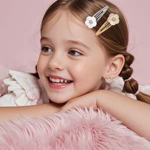 Toddler model wearing glitter flower hair clips and small hoop earrings on pink background