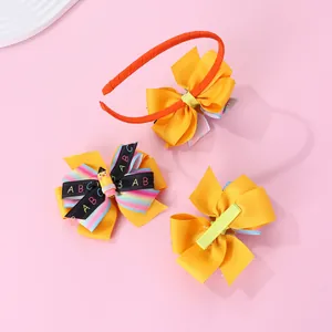 Detail of school-themed hair bow set with yellow ribbon and pencil charm on pink surface