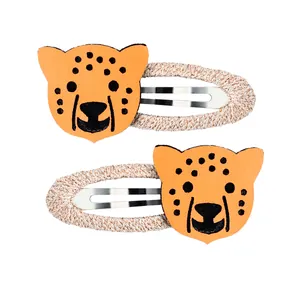 Détail de deux barrettes léopard en cuir orange avec une base en tissu tressé beige