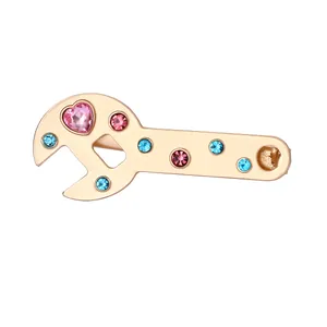 Macro detail of wrench-shaped hair clip with pink heart and blue crystals in gold