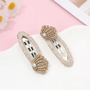 Close-up of shell shaped hair clips with sequins and pearl on beige woven fabric