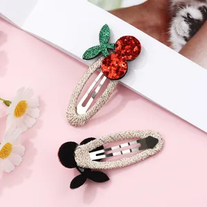 Detailed view of cherry-shaped hair clips featuring red glitter sequins and woven gold wraps