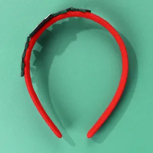Dettaglio del cerchietto natalizio in peluche rosso con decoro verde su sfondo verde