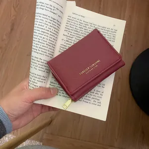 Handheld wine red Saffiano leather trifold wallet with gold lettering and zipper detail
