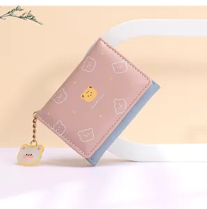 Detalle de billetera bicolor rosa y azul con estampado de oso y amuleto colgante