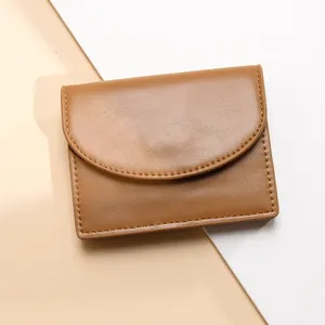 Cartera pequeña plegable de cuero marrón con solapa curva sobre fondo bicolor