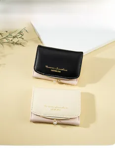 Detail of short leather wallets in black and beige with gold trim and pearl charms
