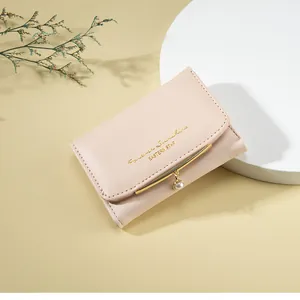 Close-up of pink minimalist leather wallet with gold trim and delicate pearl pendant