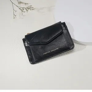 Détail du mini portefeuille en cuir noir texturé avec lettrage doré et fermeture éclair métal