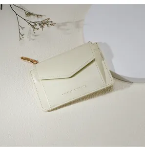Détail d'un porte-cartes en cuir crème avec fermeture éclair dorée et texte gravé