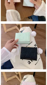 Detail of short leather wallet featuring 3D bear embossment and soft pom-pom keychain