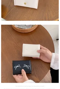 Detail of bow-knot wallets with pearl accents in cream and black on a wooden table