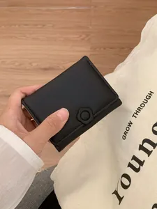Minimalist black tri-fold mini wallet with floral buckle held in hand for daily use