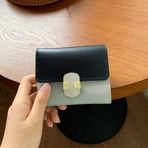 Short two-tone leather wallet for women with gold clasp on wooden background