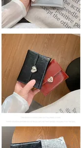 Detail of heart-shaped metal buckle on folded textured wallets in multiple colors